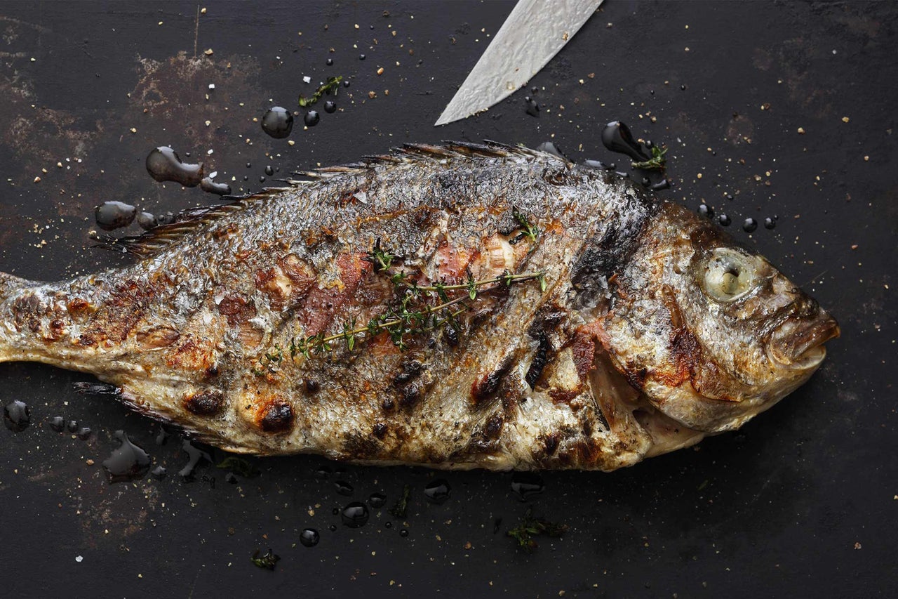 Poisson grillé avec des herbes et un couteau sur fond sombre