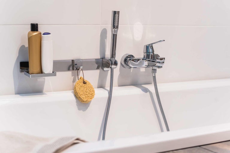 Robinet de salle de bain avec douchette, gel douche et éponge de bain sur une baignoire