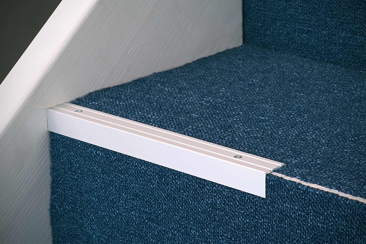 Detailaufnahme einer Treppenstufe mit blauem Teppich und Treppenkantenprofil aus Metall