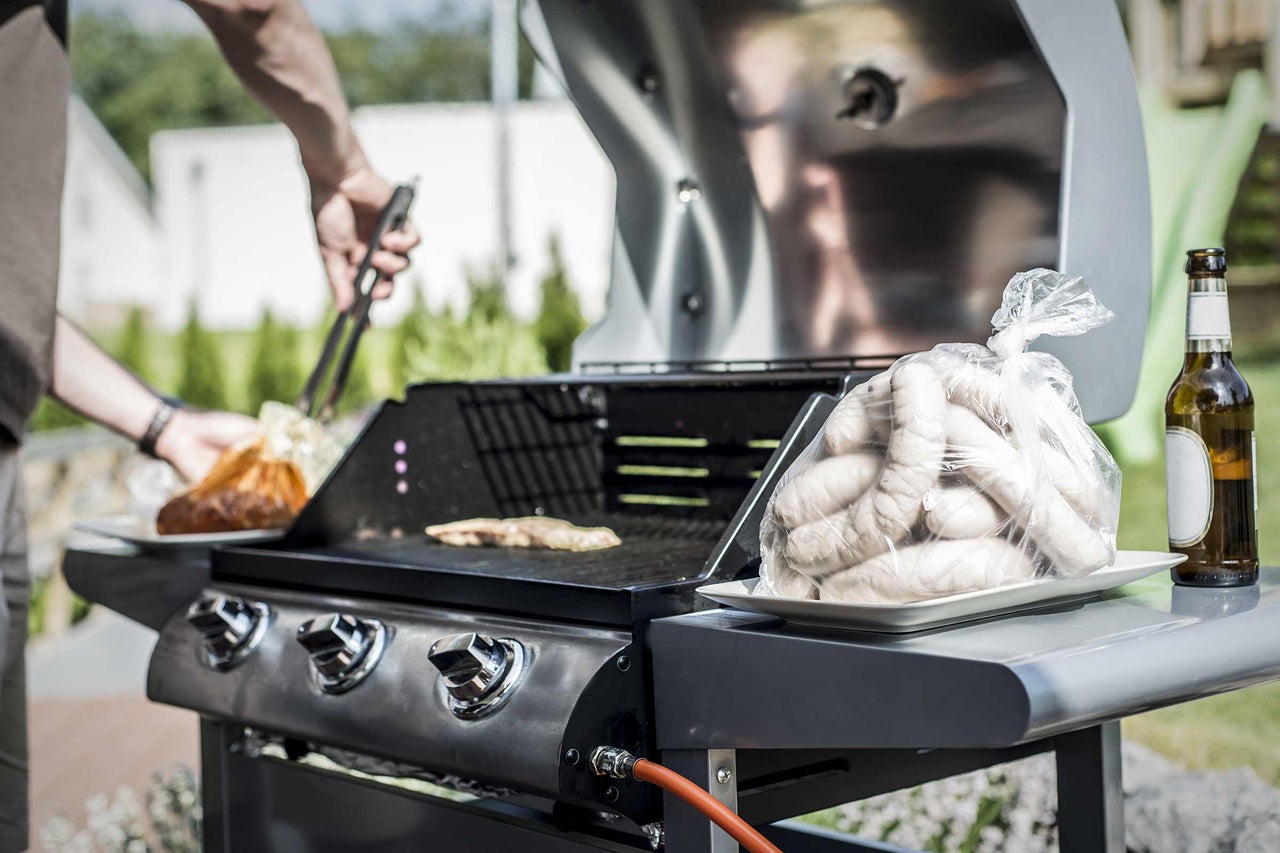 Grillszene mit Grill, Würstchen und Person mit Grillzange