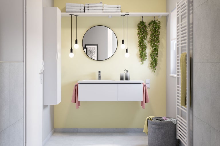 Salle de bains moderne et lumineuse avec meuble sous-vasque blanc, miroir rond, quatre suspensions, armoire haute et radiateur sèche-serviettes.