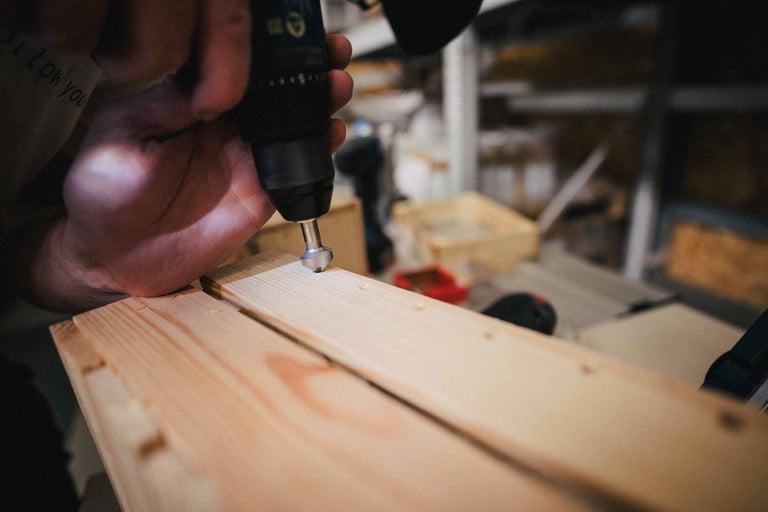 Une personne utilise une perceuse pour percer un trou dans une planche de bois.