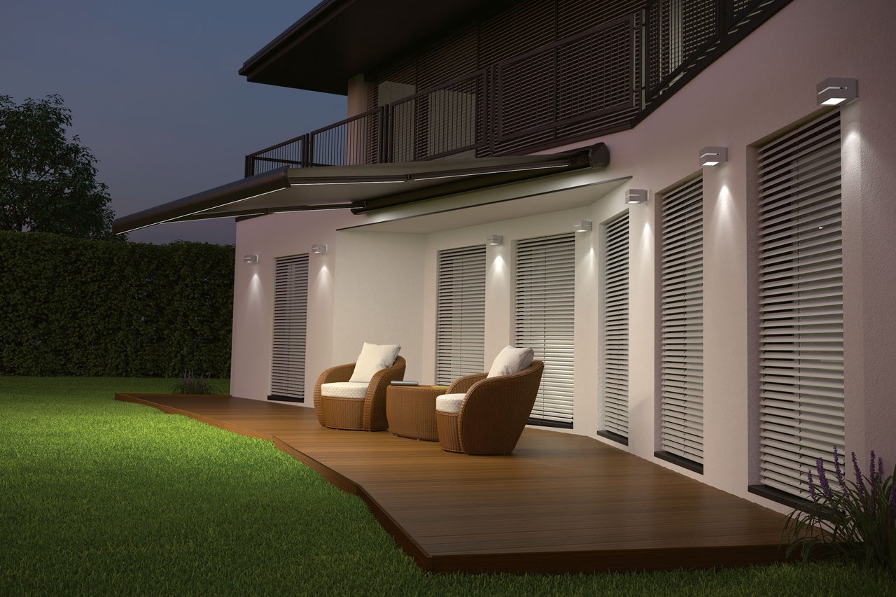 Façade de maison avec store, éclairage extérieur et salon de jardin sur terrasse en bois