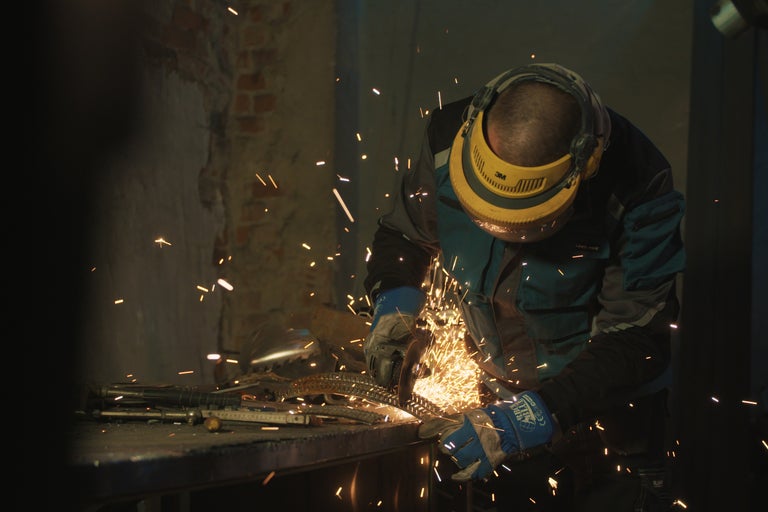 Homme avec casque de protection travaillant le métal avec une meuleuse d'angle, produisant des étincelles.