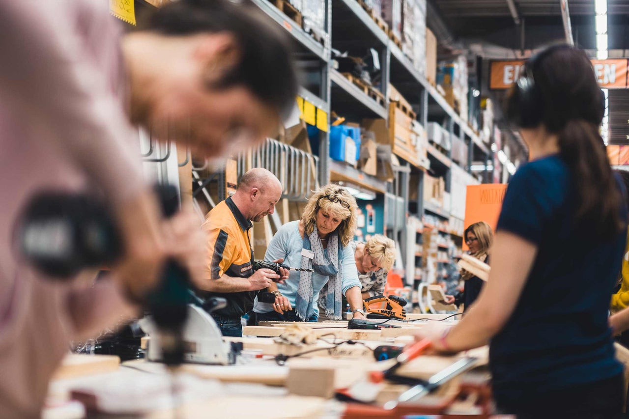 Personen arbeiten mit Elektrowerkzeugen an einer Werkbank in einem Hornbach Markt.