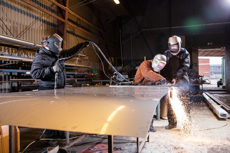 Trois personnes soudent du métal dans un atelier avec des casques de soudure