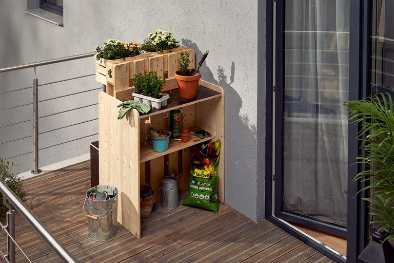 Scène de jardin avec table de plantation en bois, jardinières, plantes et outils de jardin sur un balcon