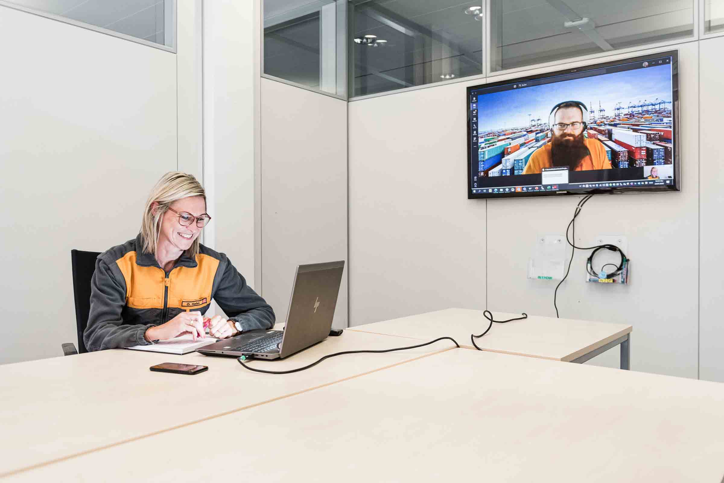 Une femme est assise à une table et a une conversation vidéo sur un écran au mur.