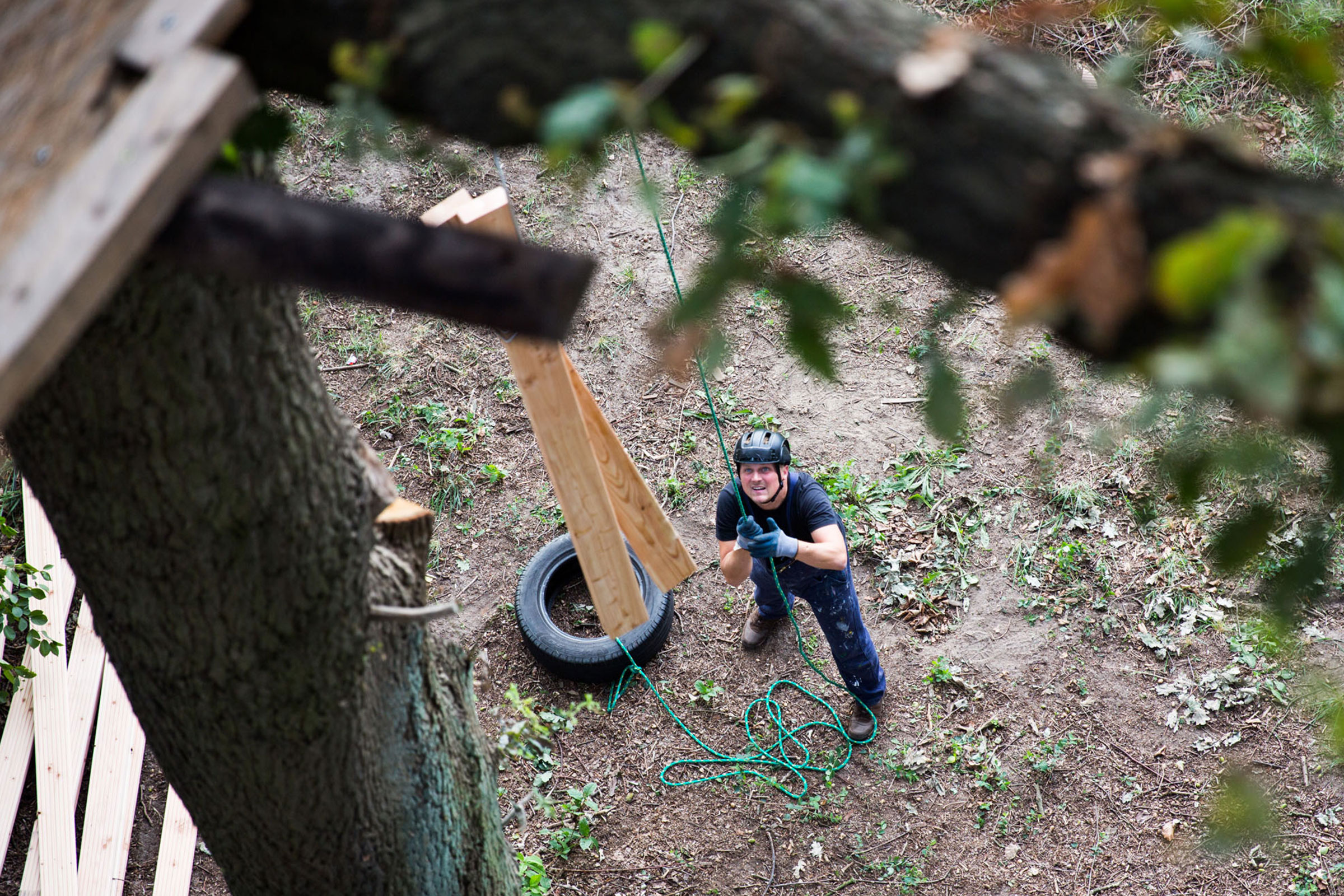 Mann mit Helm baut Baumhaus mit Holz und Seil