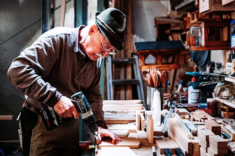 Un homme travaille avec une perceuse-visseuse sans fil sur une pièce de bois dans un atelier.