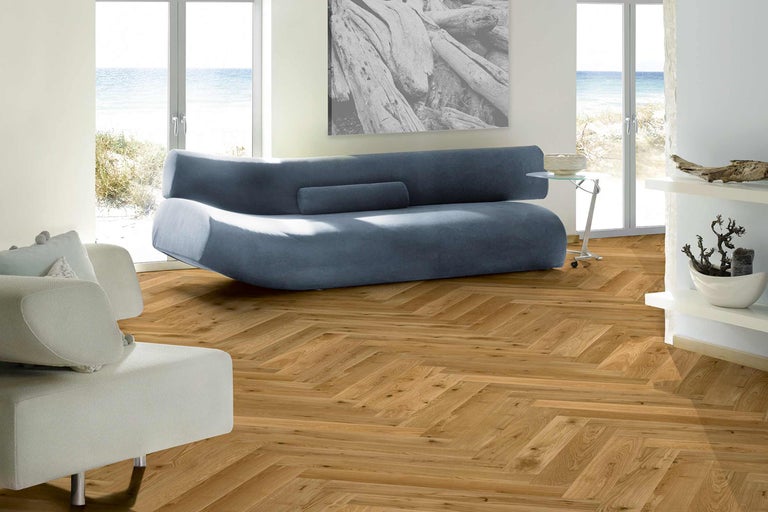 Salon lumineux avec parquet à chevrons, canapé et fenêtres