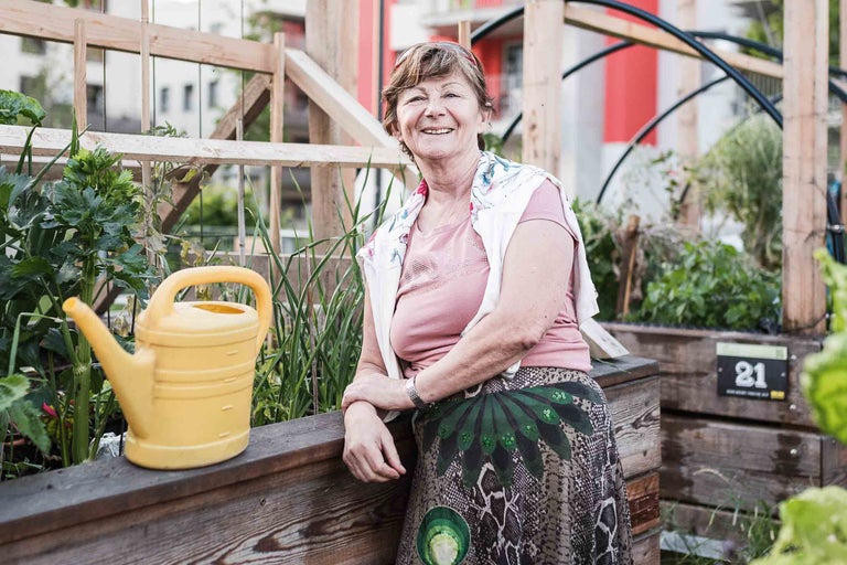 Femme dans un jardin urbain avec un potager surélevé et un arrosoir jaune