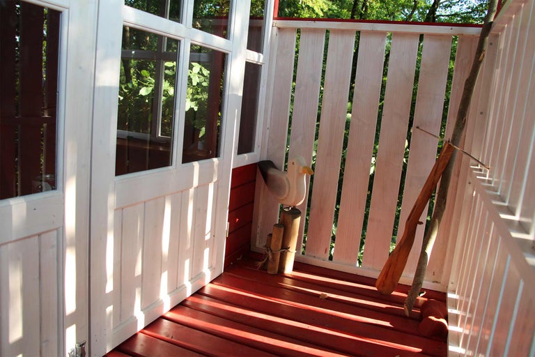 Innenansicht eines Spielhauses mit Holzboden, Fenster, Holzzaun und Dekoration