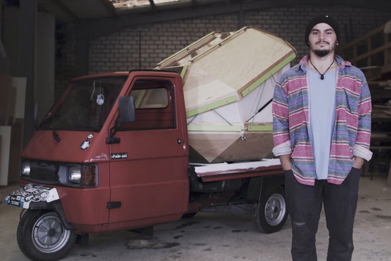Petit camion de livraison avec superstructure en bois et une personne posant dans un atelier.