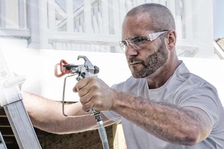 Un homme portant des lunettes de protection utilise un pistolet à peinture pour des travaux de peinture.