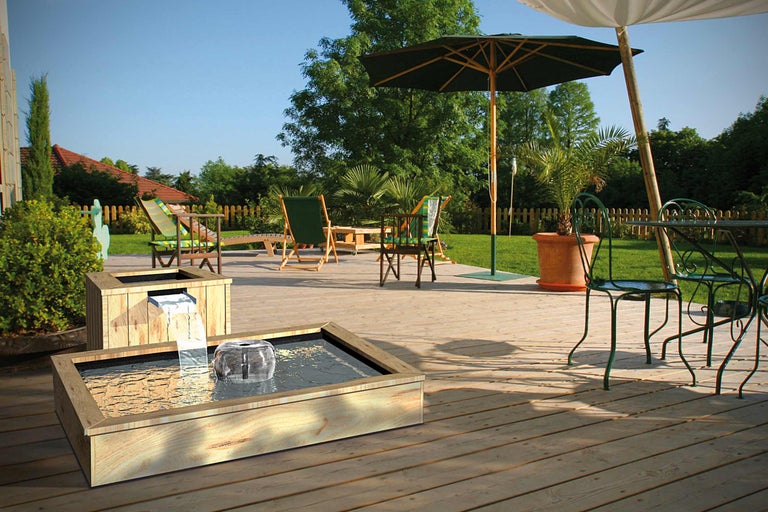 Gartenszene mit hölzernem Wasserspiel, Gartenmöbeln und Sonnenschirmen auf einer Holzterrasse