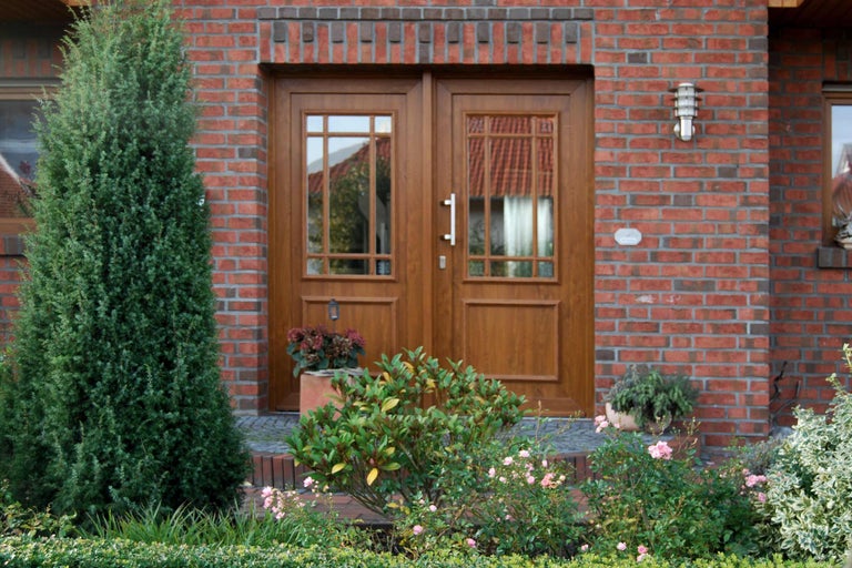 Doppeltür aus Holz mit Glaseinsätzen in einer roten Backsteinfassade umgeben von Pflanzen