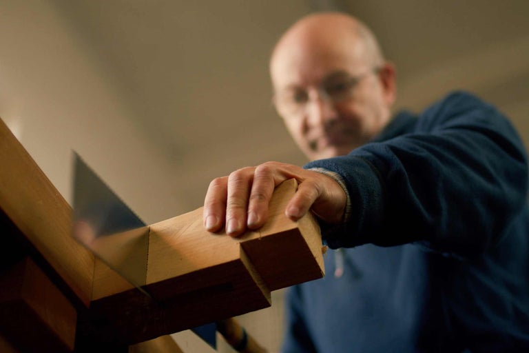 Un homme scie du bois à l'aide d'une scie et d'une boîte à onglets