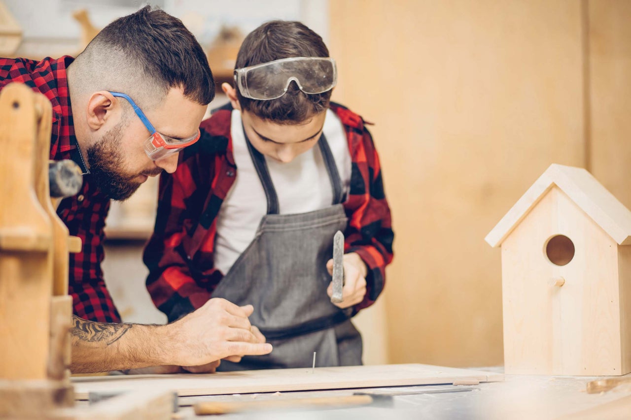Père et fils construisent ensemble une cabane à oiseaux avec un marteau et un clou.