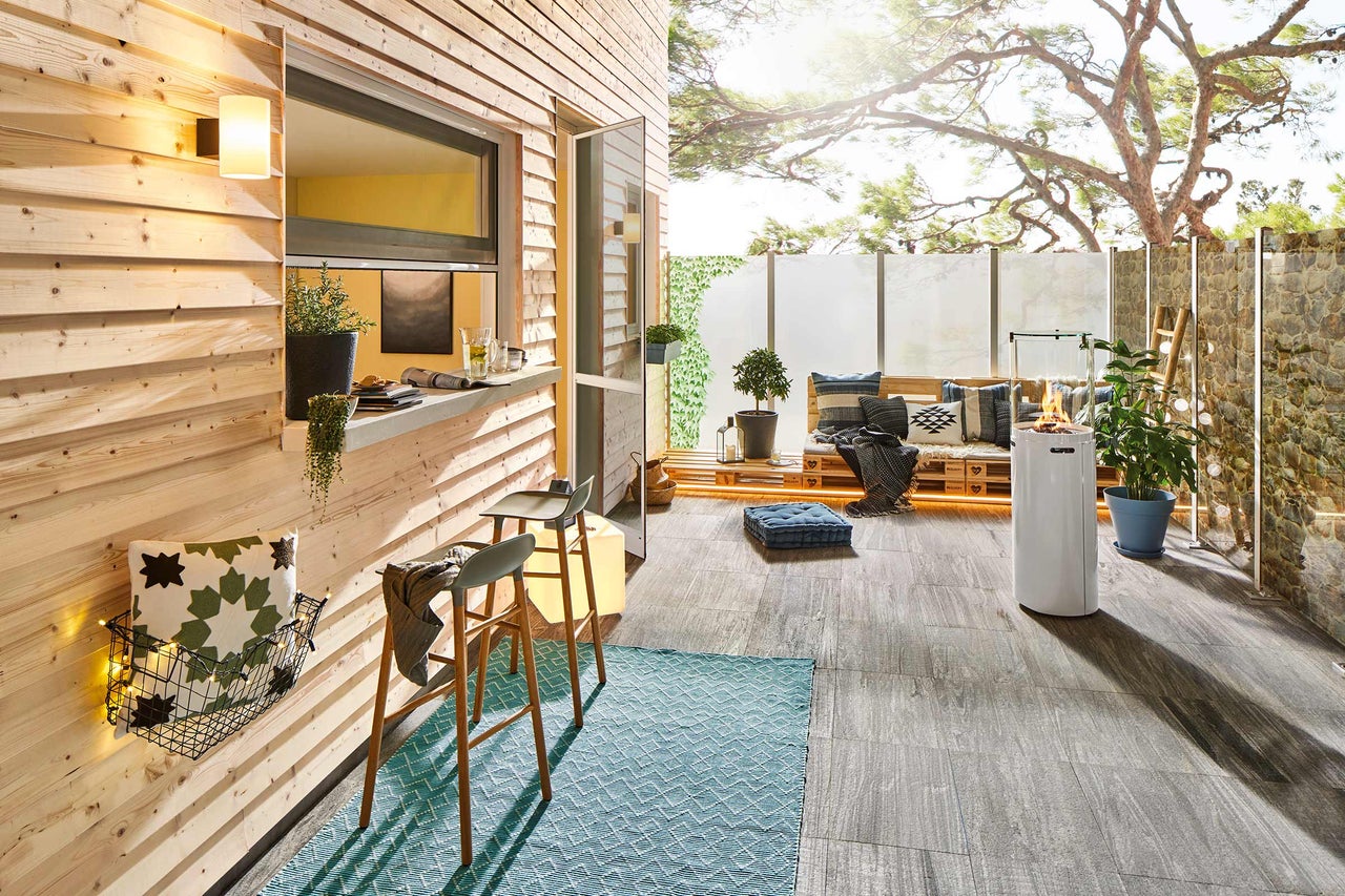 Terrasse lumineuse avec bardage en bois, tabourets de bar, tapis, sièges en palettes et cheminée extérieure