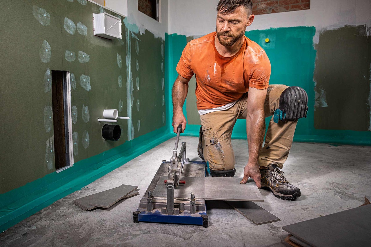 Fliesenleger bei der Arbeit mit Fliesenschneider im Badezimmer