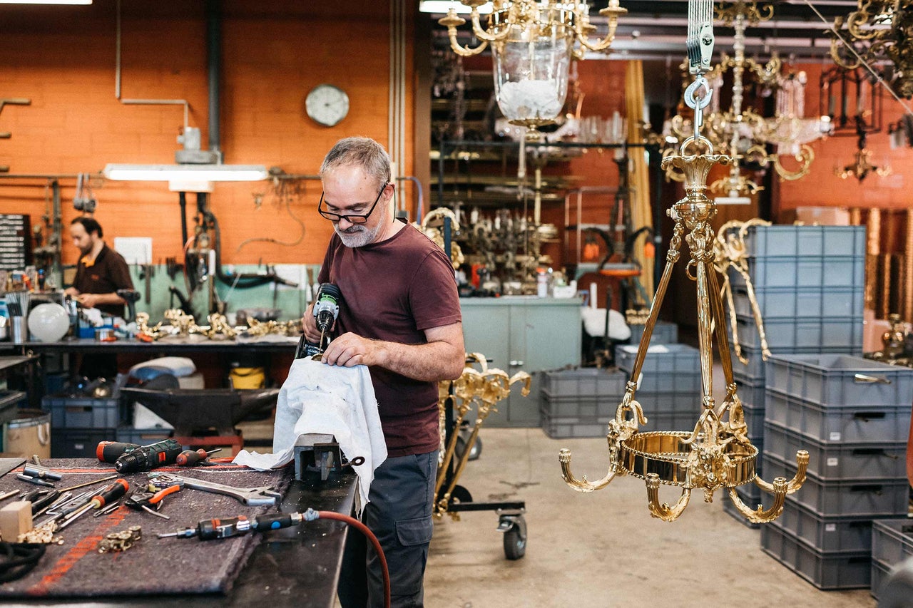 Mann arbeitet an einem goldenen Kronleuchter in einer Werkstatt mit Werkzeugen.