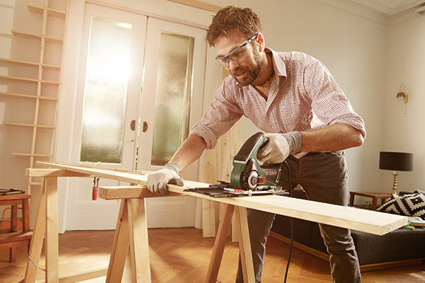 Un homme scie une planche de bois avec une scie circulaire à main sur un établi.