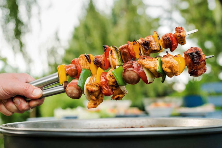 Zwei Grillspieße mit Fleisch und Gemüse werden über einem Grill gehalten.