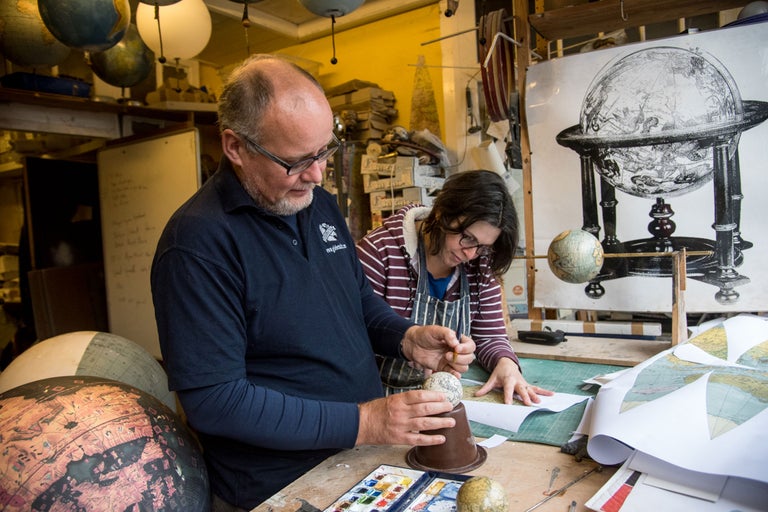 Deux personnes travaillent dans un atelier sur des globes et des cartes