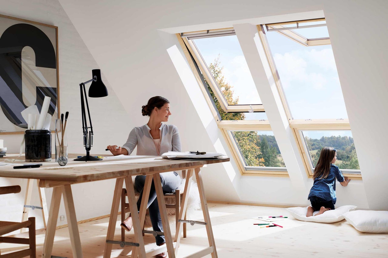 Heller Dachboden mit Dachfenstern, Frau am Schreibtisch und Kind am Fenster