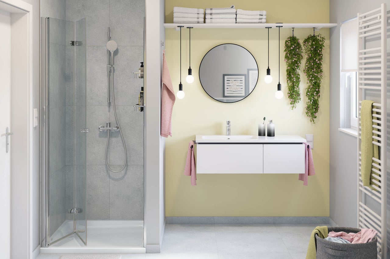 Salle de bains moderne et lumineuse avec douche en verre, meuble sous-vasque suspendu blanc, miroir rond, quatre suspensions et un sèche-serviettes.
