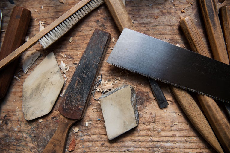 Divers outils tels qu'une scie, une pierre à aiguiser, une brosse et un ciseau sur une surface en bois.