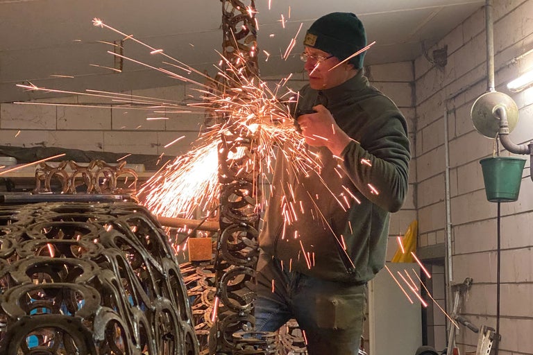 Ein Mann bearbeitet ein Metallobjekt mit einem Winkelschleifer, wobei Funken sprühen.