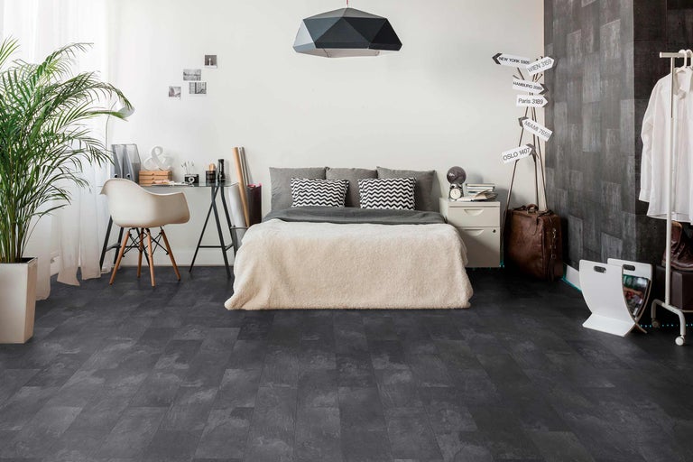 Schlafzimmer mit Bett, Schreibtisch und dunklem Bodenbelag in Steinoptik.