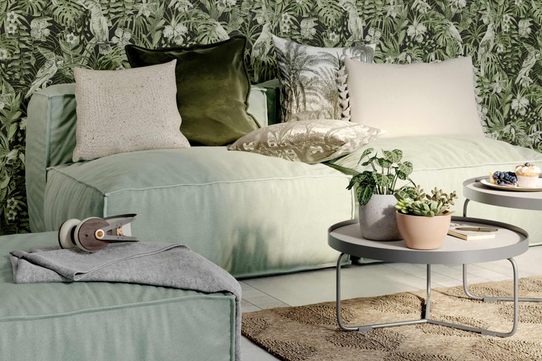 Wohnzimmer mit Sofa, Kissen, Beistelltisch und Zimmerpflanzen vor einer gemusterten Tapete