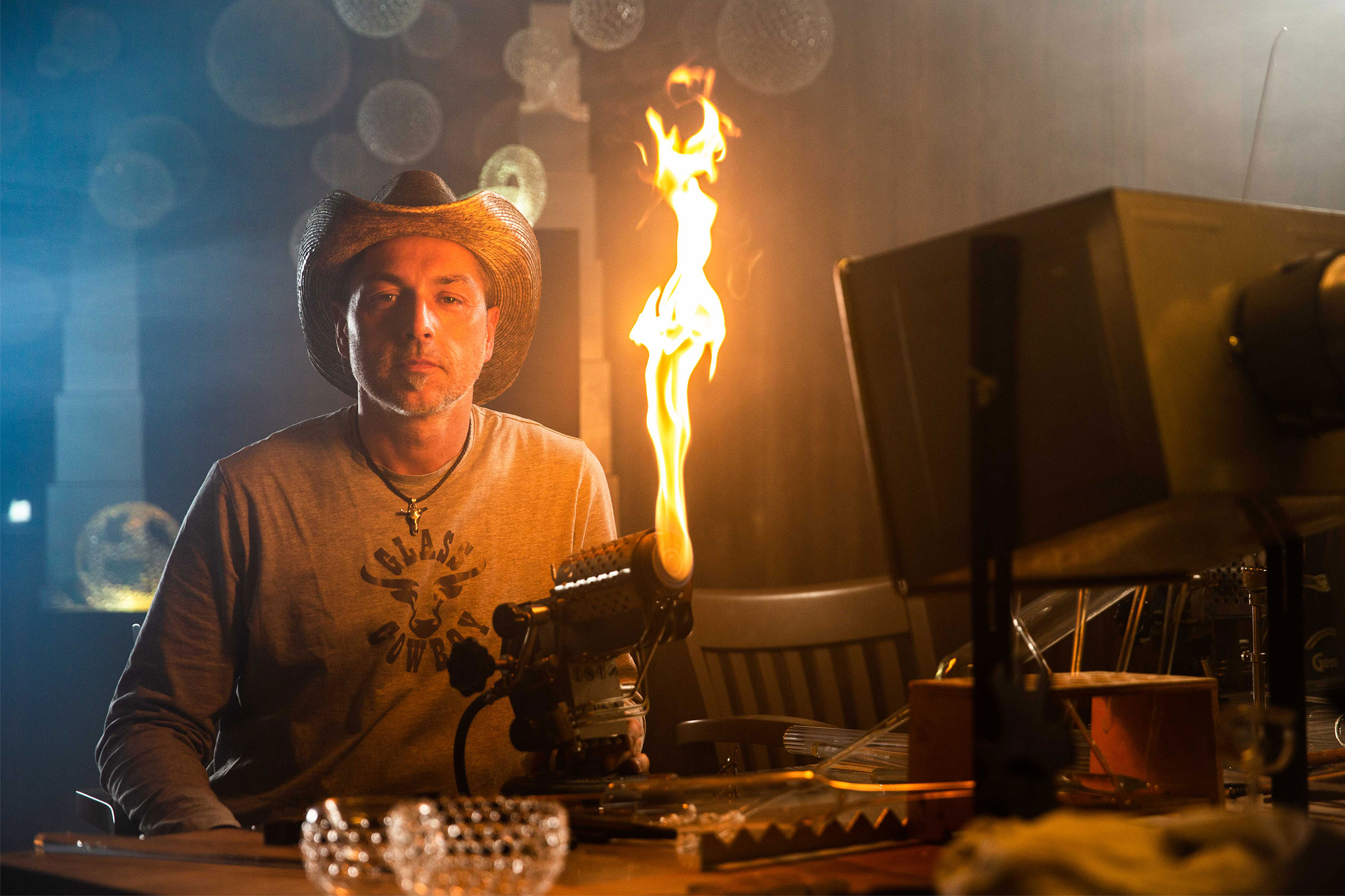 Homme avec un chapeau de cowboy utilisant un chalumeau pour le travail du verre.