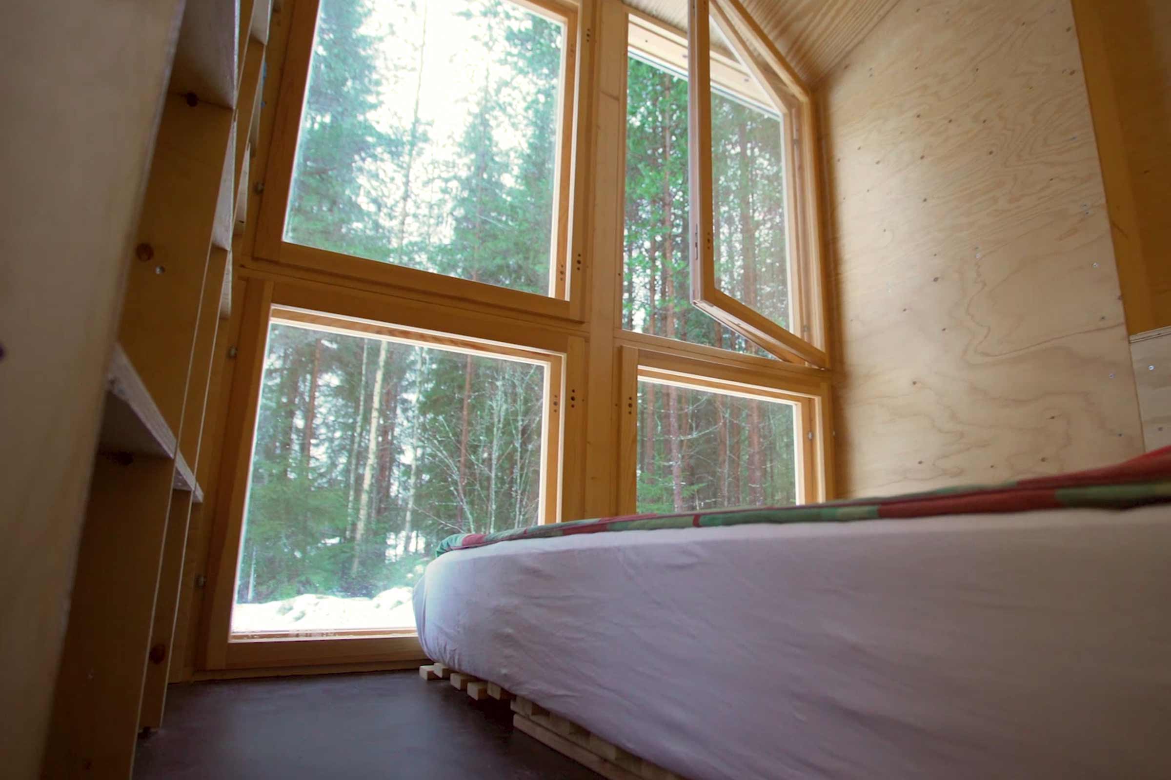 Intérieur d'une pièce avec un lit et des fenêtres en bois donnant sur des arbres.