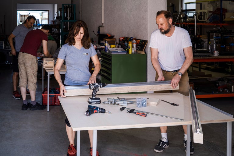 Des personnes travaillent avec des perceuses, des vis, des serre-joints et du bois sur un établi.