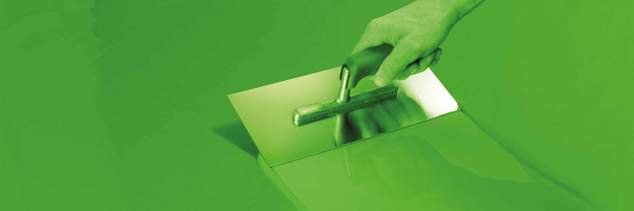 Eine Hand hält eine Glättkelle beim Auftragen von Estrich.