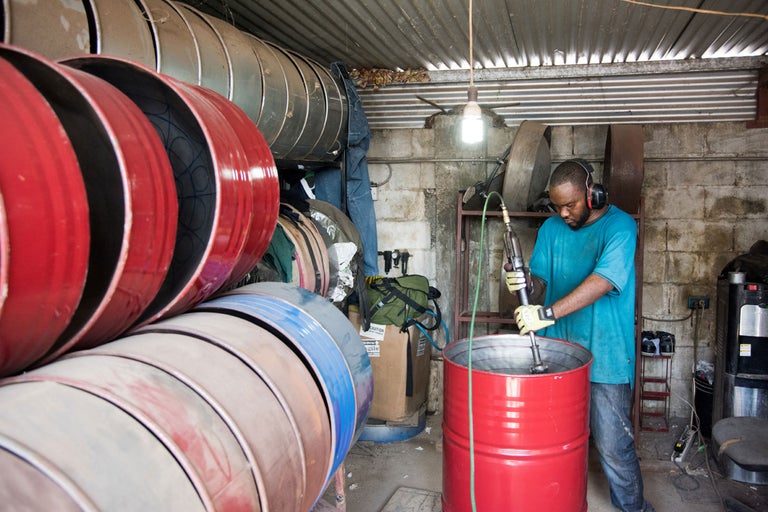 Homme portant un casque utilisant un mélangeur de peinture dans un fût métallique dans un atelier