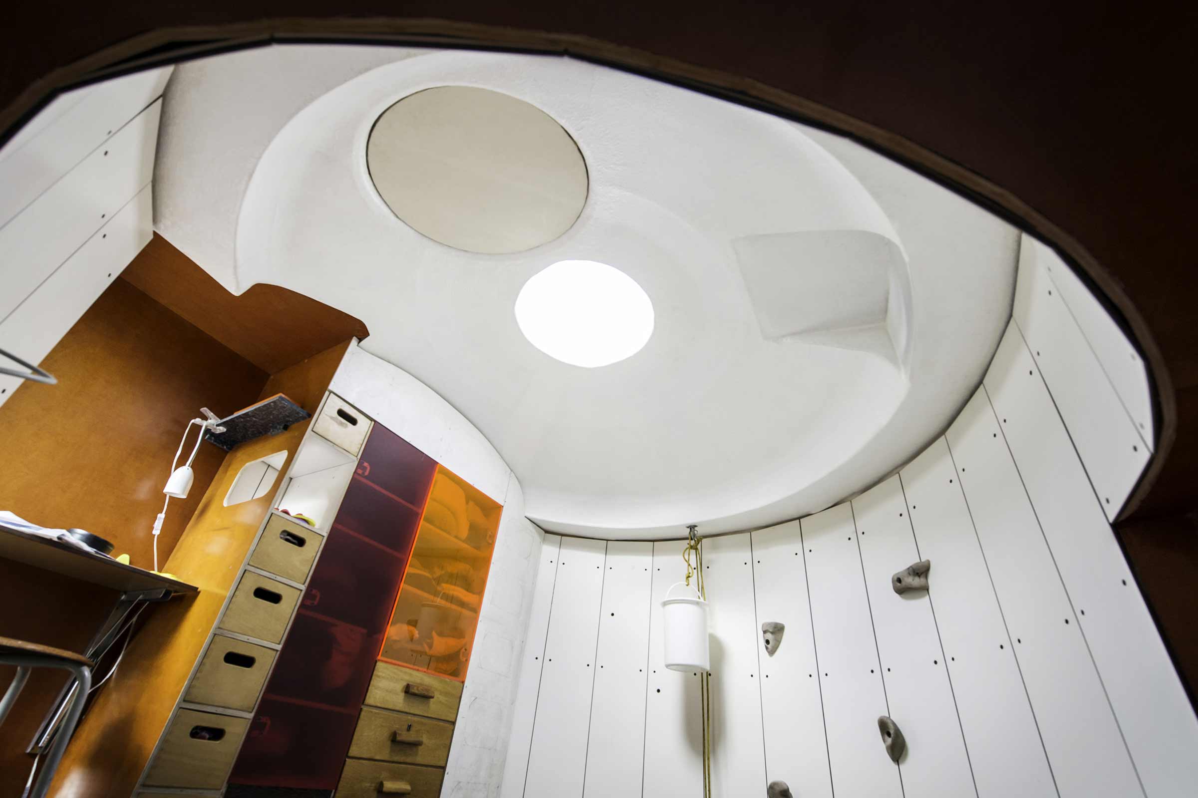 Innenansicht eines Zimmers mit Kletterwand, Schreibtisch und eingebauten Schränken unter einer gewölbten Decke mit Oberlicht