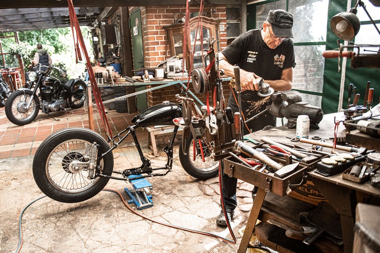 Atelier avec moto, établi et artisan au travail.