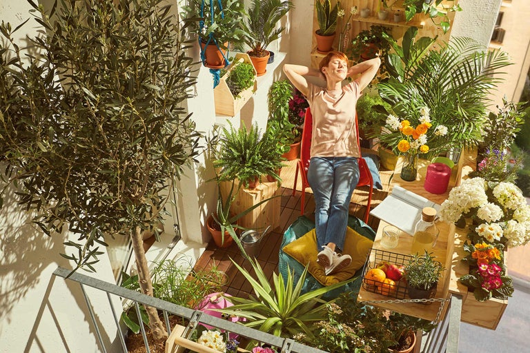 Une femme se détend sur un balcon verdoyant avec des plantes en pot et des jardinières.