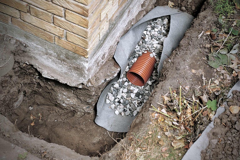 Drainagegraben mit Drainagerohr und Kies zum Schutz eines Gebäudes.