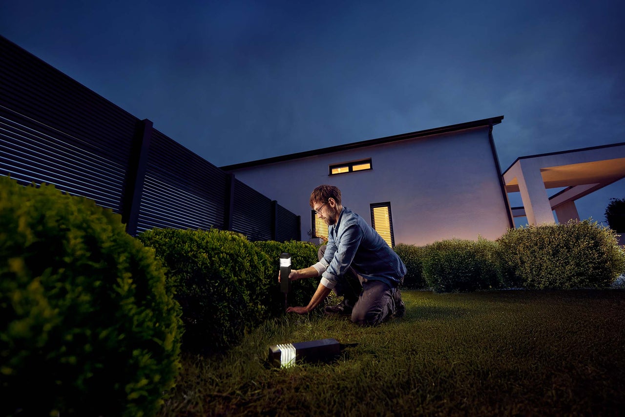 Un homme installe des lampes de jardin dans le jardin.