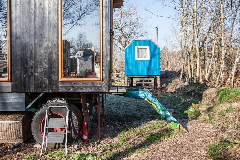 Scène avec une caravane à revêtement en bois et une petite maison à l'arrière-plan.