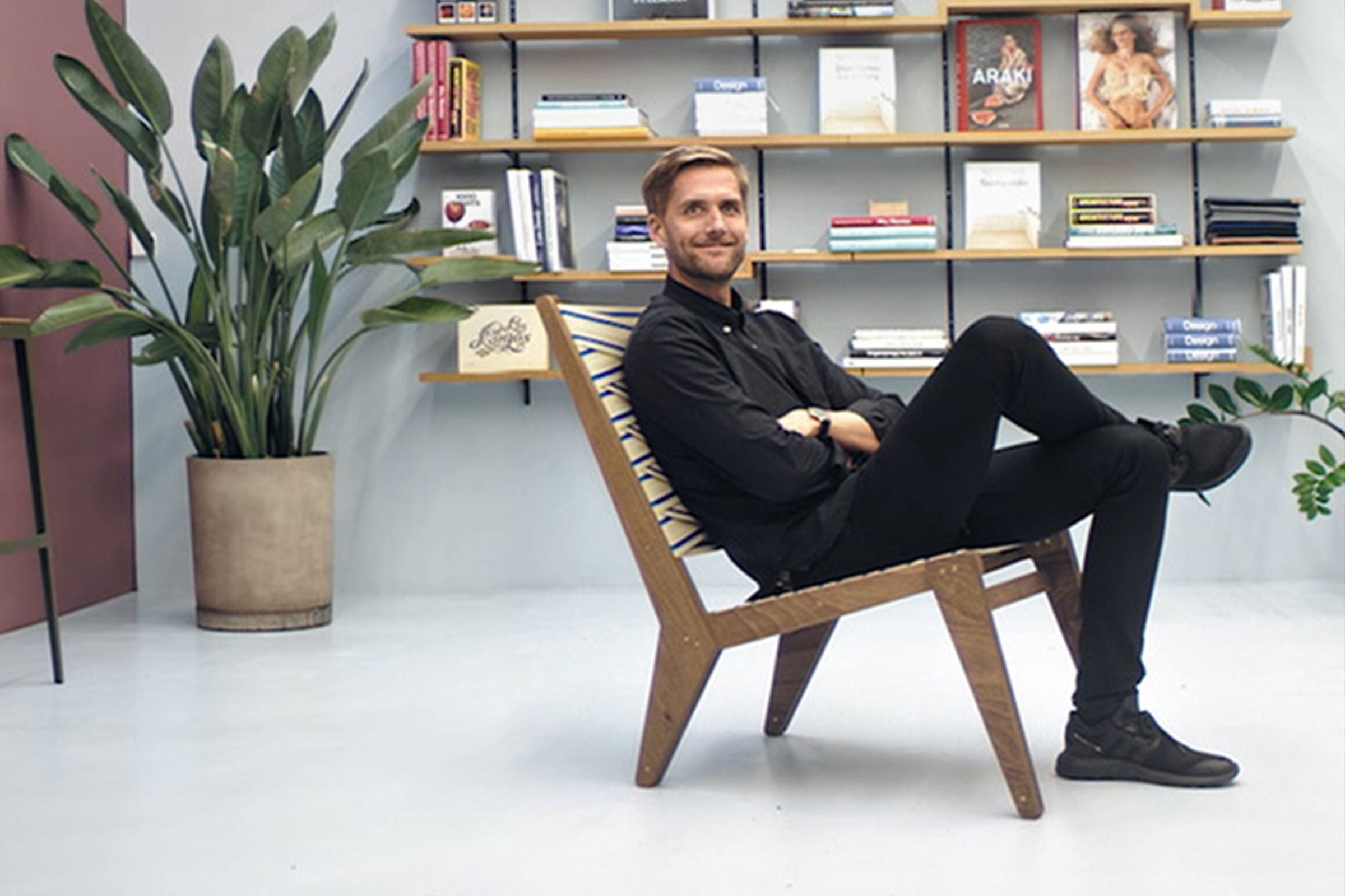 Un homme est assis sur une chaise en bois devant une bibliothèque et une plante d'intérieur.