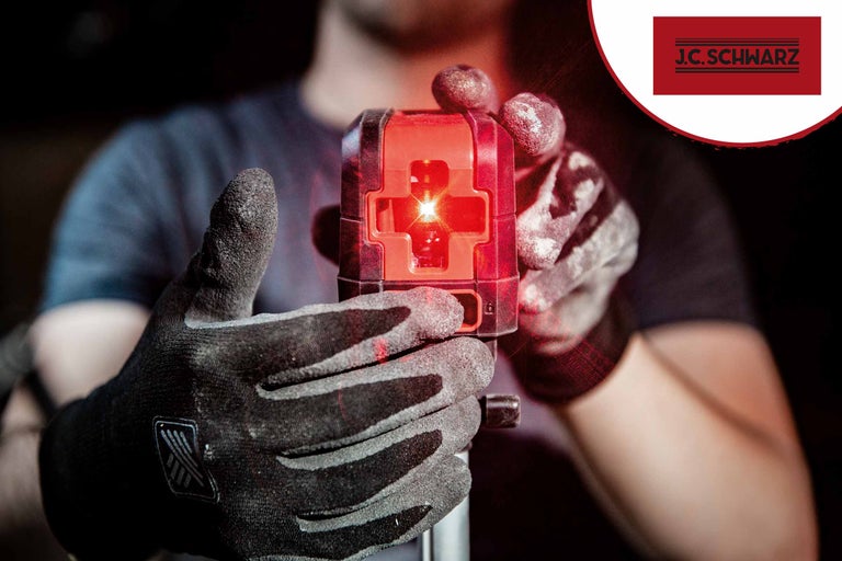 Une personne tient un laser lignes croisées avec des gants. Logo J.C. Schwarz.