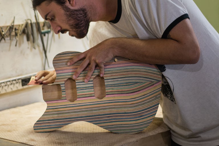 Un homme ponce un corps de guitare en bois multicolore.