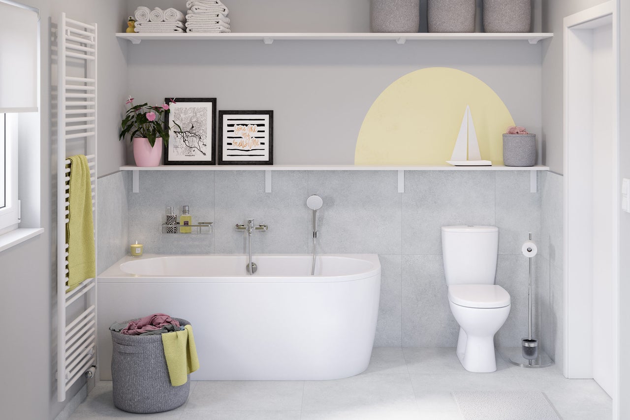 Salle de bains moderne lumineuse avec baignoire blanche, WC à poser, sèche-serviettes sur carrelage gris et deux étagères murales décorées.